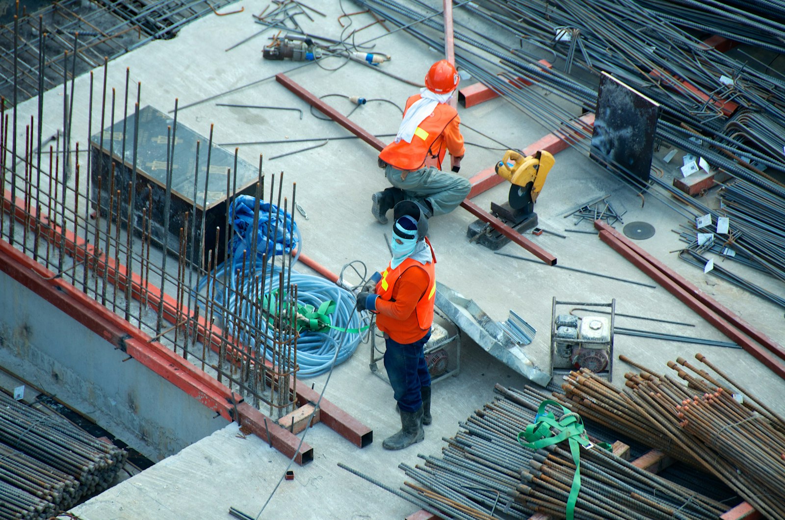 Two construction workers in orange hi-vis vests and hard hats working among steel reinforcing