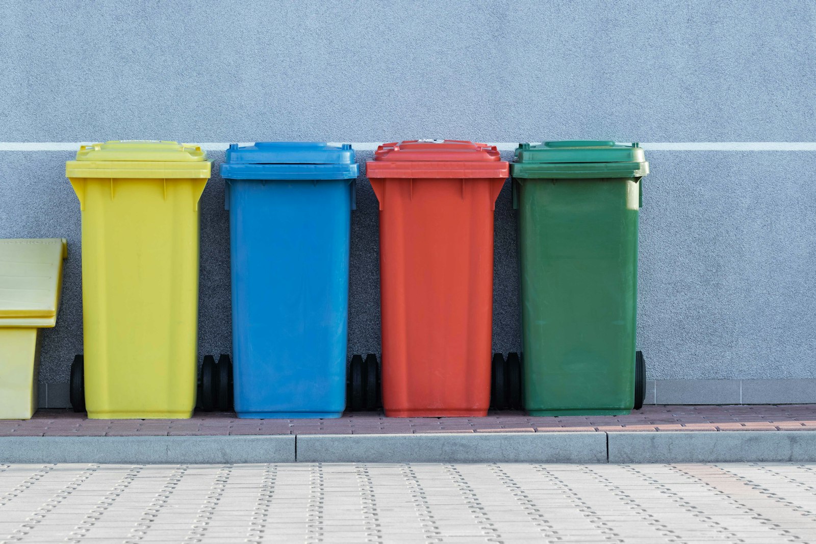 Row of yellow, blue, red and green household wheelie bins against a concrete wall