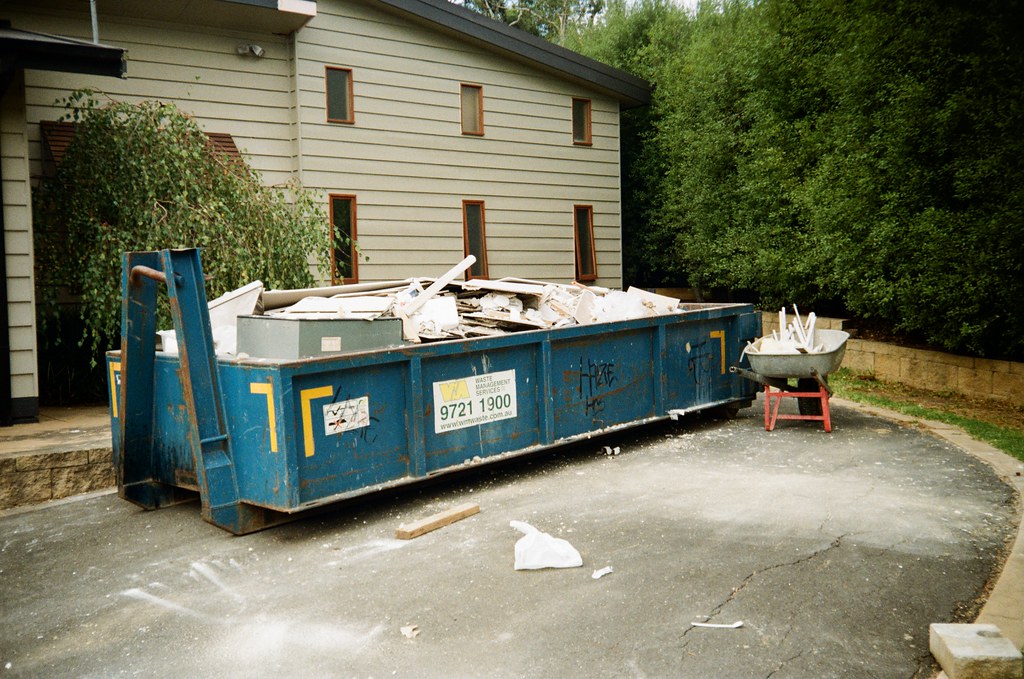 Blue hook-lift skip bin filled with renovation offcuts parked in a residential driveway